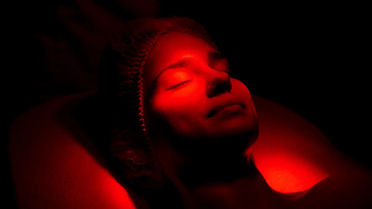 A woman getting facial red light therapy in a dark room